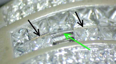 A ring with two middle rows of square stones in invisible setting. One stone has fallen out. The green arrow points to the usually invisible 'rail' on which the stones click. The black arrows point at evidence of an earlier repair attempt. The yellowish substance between the stones is glue.